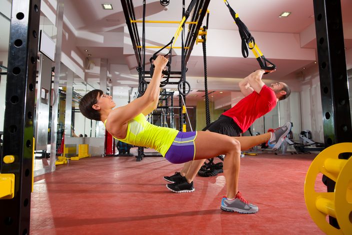 Man and woman training TRX fitness exercises at the gym