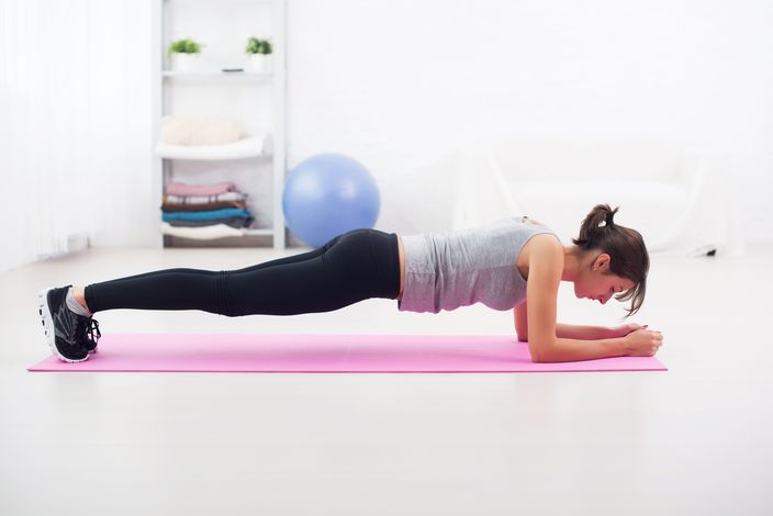 Fit girl in plank position on mat at home the