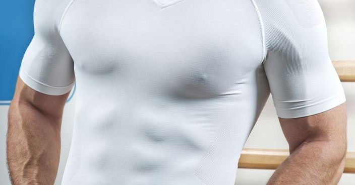 Muscular torso through white shirt in gym.