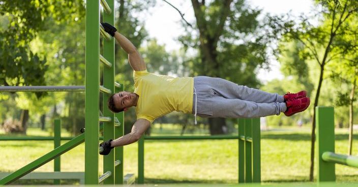 Young athlete working out in an outdoor gym, doing street workout exercises