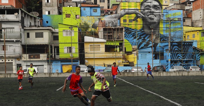 In this May 20, 2018 photo, neighborhood kids play soccer in the Jardim Peri neighborhood where professional soccer player Gabriel Jesus grew up and is featured in a mural on the side of homes in Sao Paulo, Brazil. Gabriel Jesus lived a few meters away in a modest house on Capitao Ulisses Soares de Campo street until age 16. (AP Photo/Andre Penner)