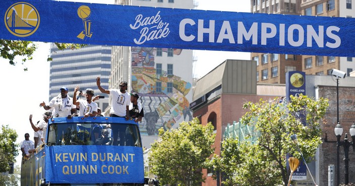 A champions banner is placed overhead as a bus carrying Golden State Warriors' Kevin Durant and Quinn Cook rides down the route during the team's NBA basketball championship parade, Tuesday, June 12, 2018, in Oakland, Calif. (AP Photo/Tony Avelar)
