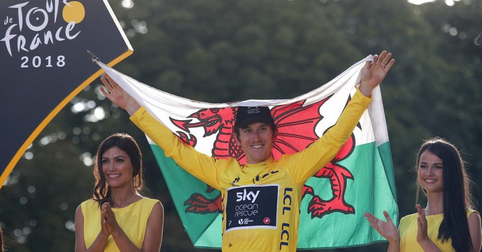Tour de France winner Britain's Geraint Thomas, wearing the overall leader's yellow jersey and holding of flag of Wales, celebrates on the podium on the Champs-Elysees avenue in Paris,, Sunday July 29, 2018. (AP Photo/Francois Mori)