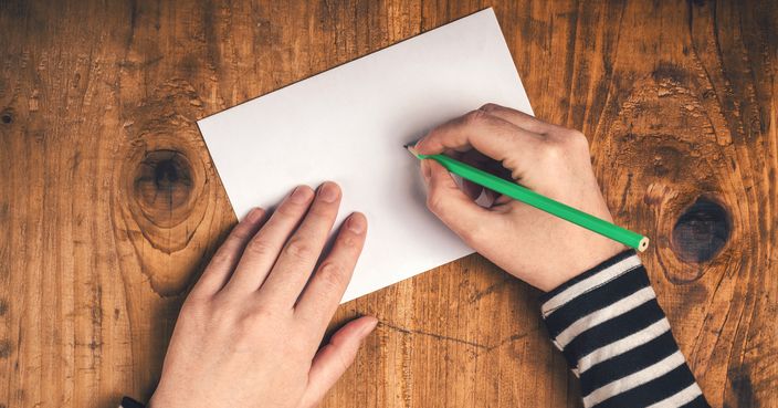 Woman writing recipient address on mailing envelope, female hands from above on office desk sending letter, top view, retro toned.