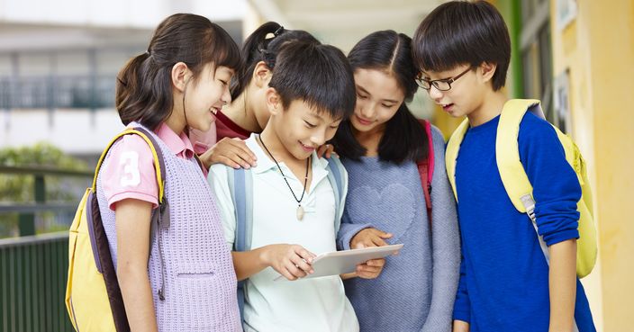 group of asian pupils looking at tablet computer in the hallway at school.