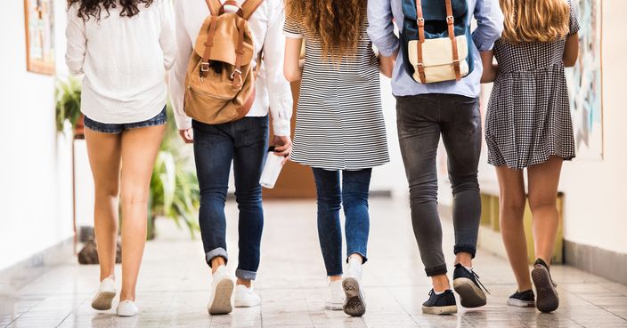 Group attractive teenage students in high school hall. Rear view.