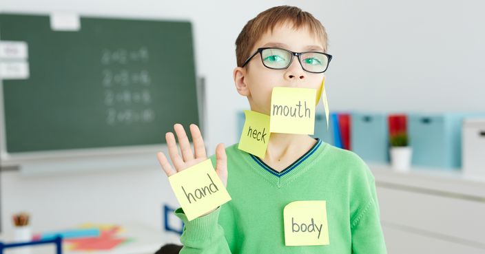 Schoolboy in eyeglasses with body part names written on notepapers stuck on his hand and face
