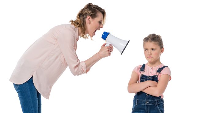 Angry mother with megaphone screaming at little daughter standing with crossed arms