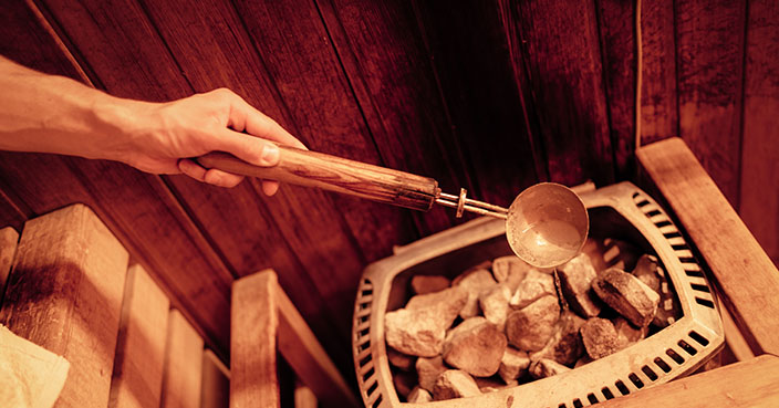 Close-up of a unrecognizable man watered hot stones in the finnish sauna.