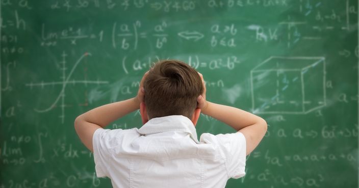 Schoolboy holding hands on his head,  getting crazy and looks at the blackboard with formulas
