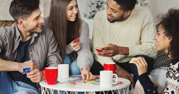 Multiracial friends having fun and playing game of cards UNO against christmas tree