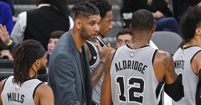 San Antonio Spurs acting head coach Tim Duncan, center, talks to Spurs forward LaMarcus Aldridge (12) as guard Patty Mills looks on during the second half of an NBA basketball game against the Portland Trail Blazers, Saturday, Nov. 16, 2019, in San Antonio. Portland won 121-116. Duncan became acting head coach after Spurs head coach Gregg Popovich was ejected after being called for two technical fouls. (AP Photo/Darren Abate)