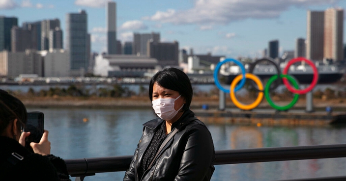 FILE - In this Jan. 29, 2020, file photo, a tourist wearing a mask poses for a photo with the Olympic rings in the background, at Tokyo's Odaiba district. Tokyo Olympic organizers repeated their message at the start of two days of meetings with the IOC: this summer's games will not be cancelled or postponed by the coronavirus spreading  neighboring China. (AP Photo/Jae C. Hong, File)
