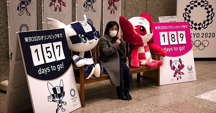 A woman removes her mask before taking pictures with the mascots of the Tokyo 2020 Olympics and Paralympics Tuesday, Feb. 18, 2020, in Tokyo. Tokyo Olympic organizers said last week there is no 