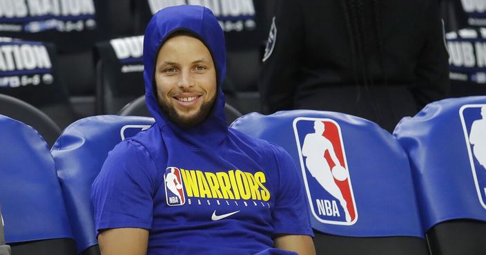FILE - In this Thursday, Feb. 27, 2020 file photo, Golden State Warriors guard Stephen Curry smiles on the bench as players warm up before an NBA basketball game between the Warriors and the Los Angeles Lakers in San Francisco. Stephen Curry had hoped to play for the Warriors on Sunday, March 1, 2020 at home against the Washington Wizards, but he won't return quite yet from a broken left hand. The two-time NBA MVP has been sidelined the past four months. (AP Photo/Jeff Chiu, File)
