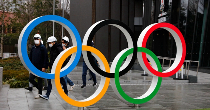 People wearing masks walk past the Olympic rings near the New National Stadium in Tokyo, Wednesday, March 4, 2020. The Tokyo Olympics are being threatened by a fast-spreading virus that has shut down most schools, sports competitions and Olympic-related events in Japan. (AP Photo/Jae C. Hong)
