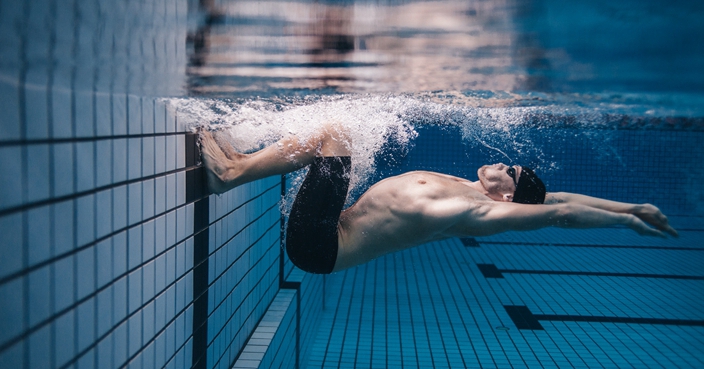 Shot of fit young man turning over underwater. Pro male swimmer in action inside swimming pool.